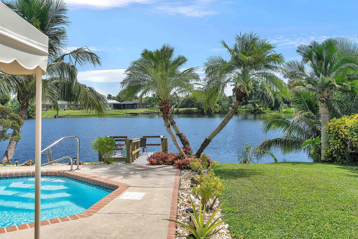 A serene outdoor space is depicted, featuring a heated saltwater pool alongside a private dock. Lush palm trees and well-maintained landscaping frame the lake view, providing a tranquil setting for relaxation and recreation.