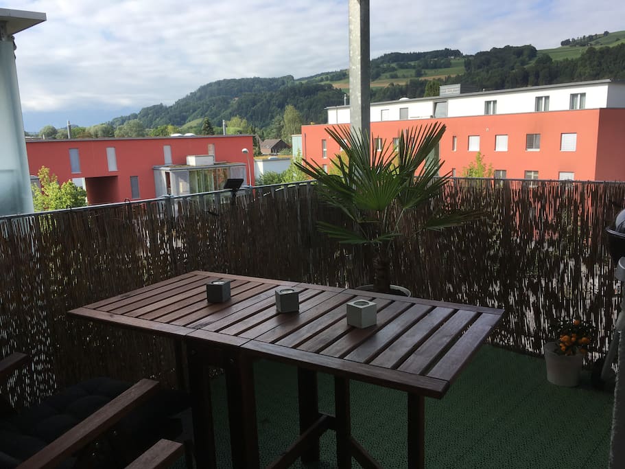 Balkon mit Tisch, Stühlen und Gasgrill, Sicht auf Alpen.