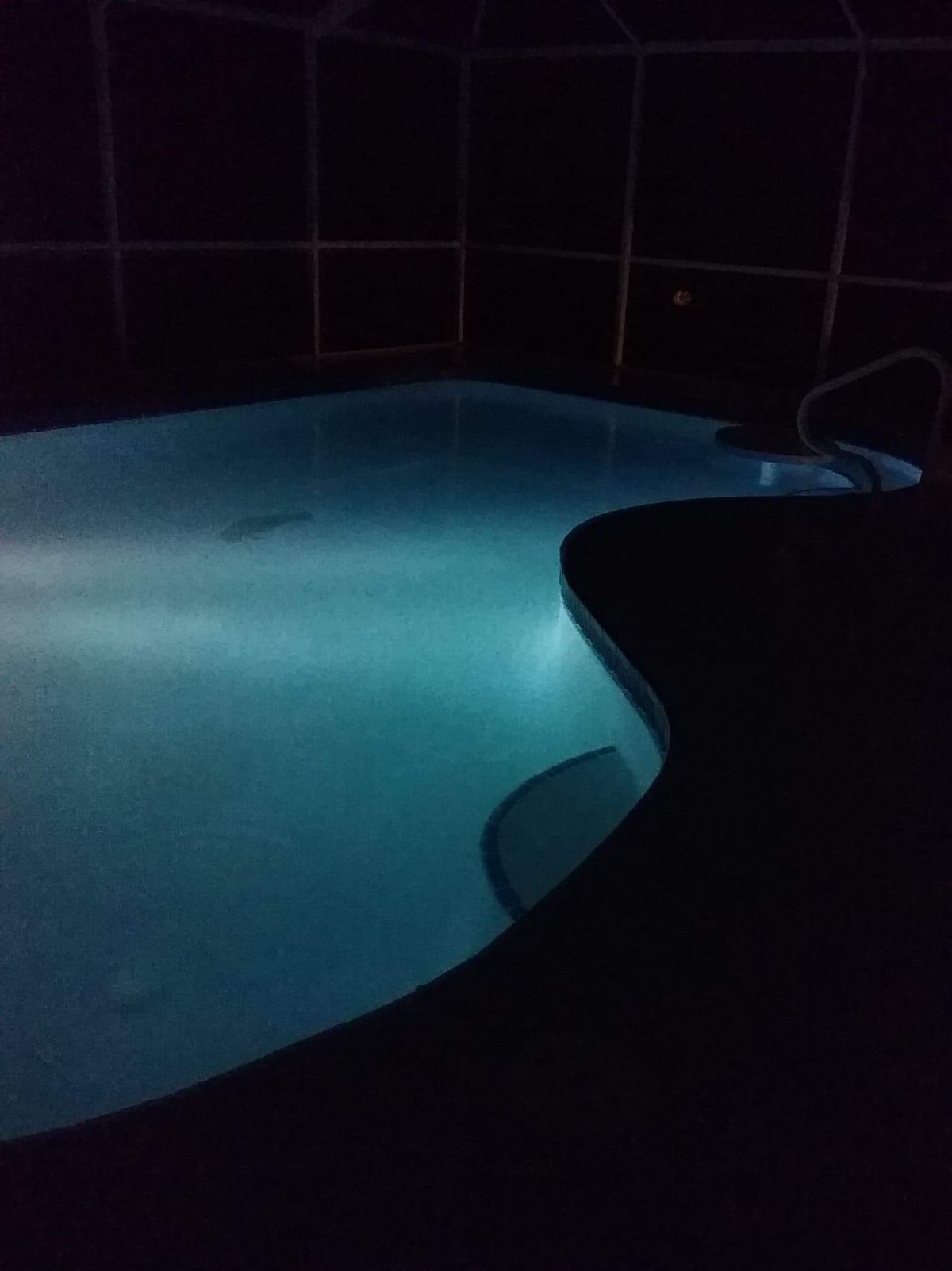 A salt-water pool is illuminated by soft lighting, creating a serene environment. The water appears calm, reflecting the glow in a softly curved design that enhances the overall tranquil ambiance. The pool area is enclosed, providing a sense of privacy.