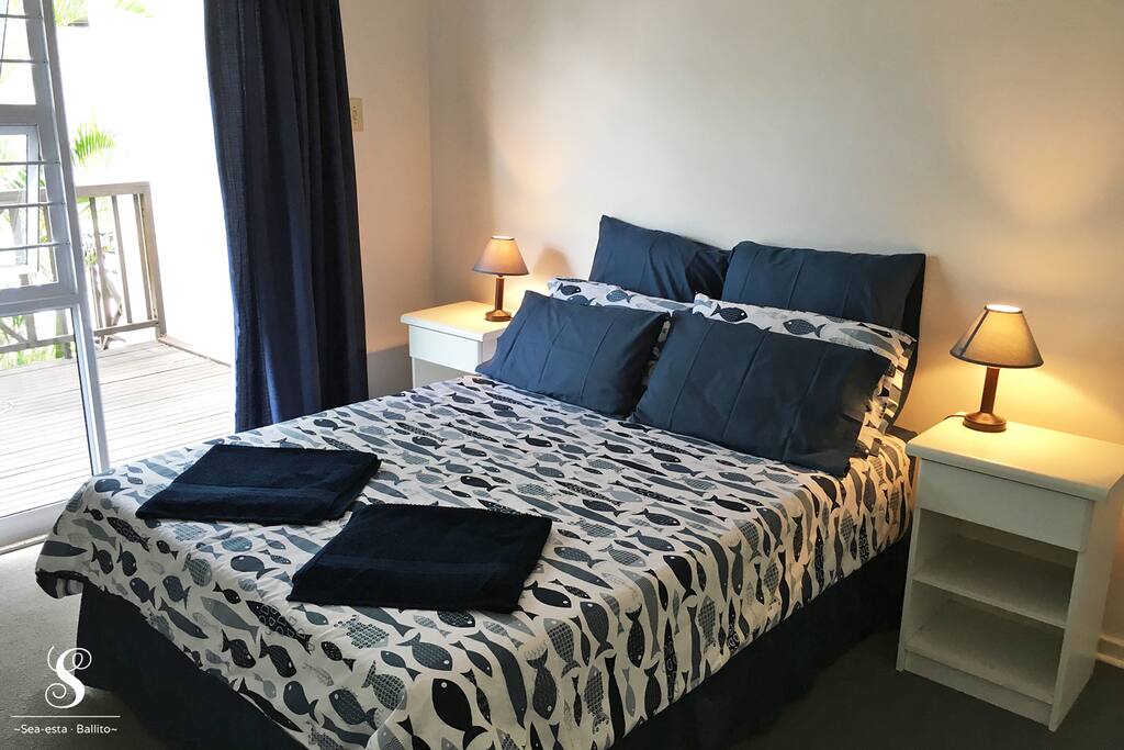 The main bedroom (upstairs) has a double bed and a door out to the wooden deck. The deck has a sea view to the right, and overlooks the small garden and the road down to the beach.