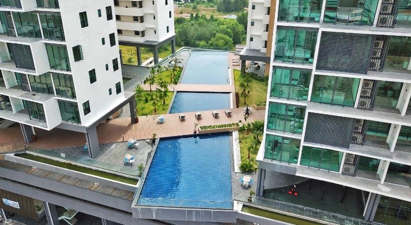 An aerial view presents a modern swimming pool area, surrounded by lush greenery and landscaped gardens. The pool features a long, rectangular design, with multiple zones for relaxation and sunbathing. Lounge chairs are positioned nearby, offering a tranquil outdoor setting.
