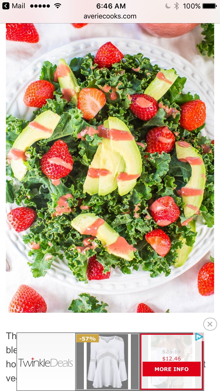 A vibrant salad is presented on a white plate, featuring a mix of fresh kale, sliced strawberries, and avocado. The colorful arrangement highlights the leafy greens alongside bright red strawberries and creamy avocado slices, creating an appealing and healthy dish.