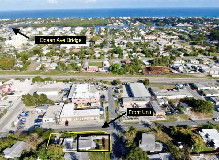 An aerial view showcases the surrounding area, highlighting the front unit's location within a community. Nearby structures, roads, and green spaces are visible, as well as a glimpse of the ocean in the background, offering insight into the property’s proximity to the beach.