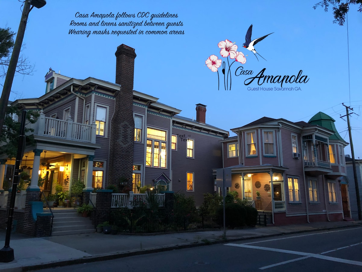 A charming Victorian home is depicted in twilight, showcasing its multi-story architecture and welcoming front porches. The image features subtle lighting that highlights the intricate details of the building’s exterior, along with greenery lining the street, creating a serene urban environment.