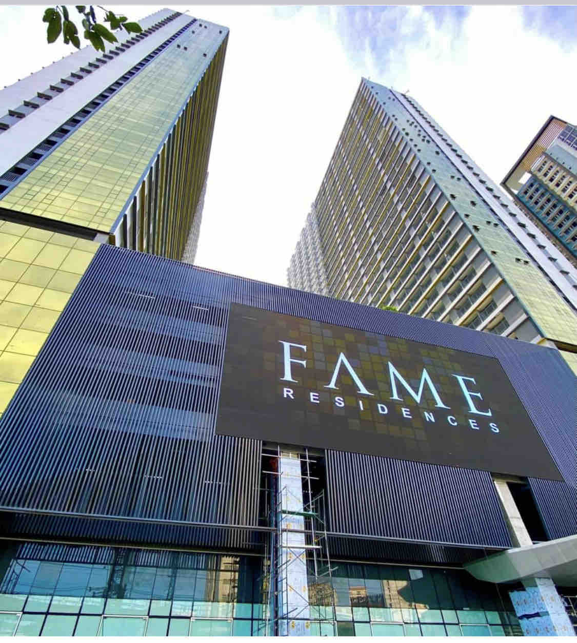 The exterior view of Fame Residences showcases a modern architectural design, featuring two tall towers with glass facades reflecting natural light. A prominent sign displaying 'FAME RESIDENCES' is positioned at the entrance, providing a clear focal point of the building's identity.