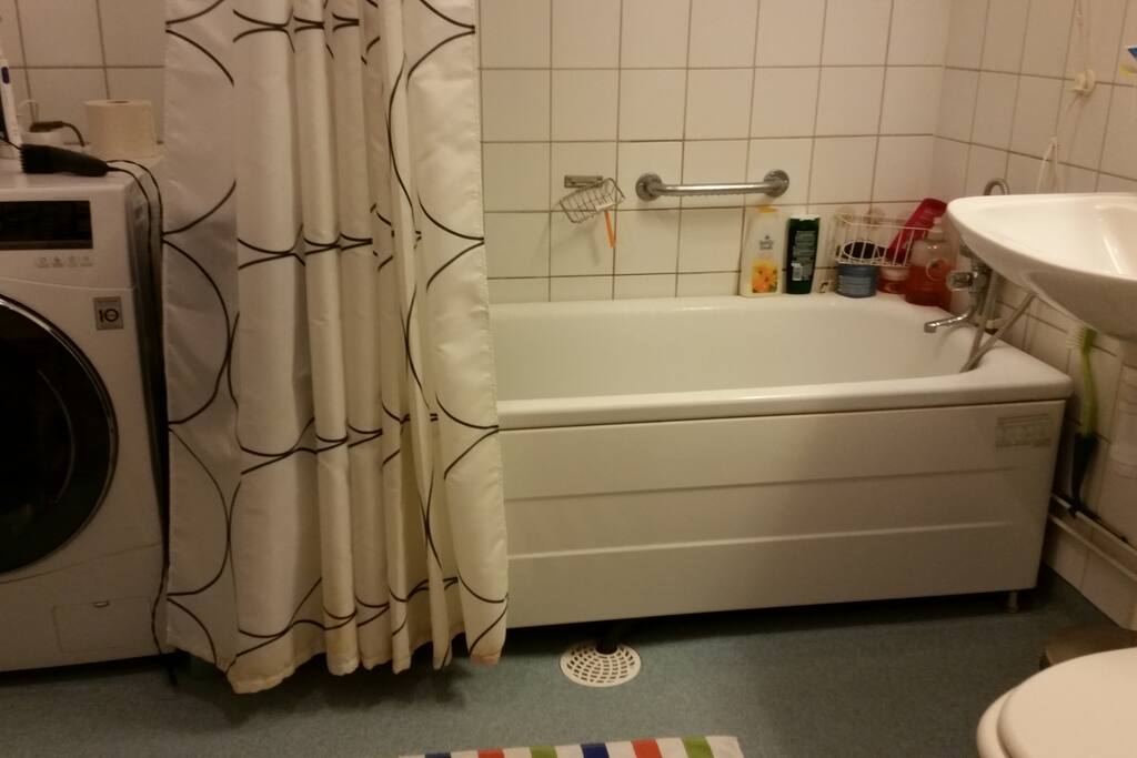 Badrum med wc, badkar och tvättmaskin. Halvkaklat.