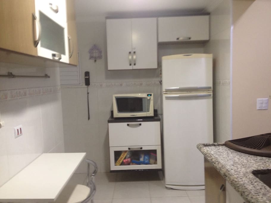 Cozinha equipada com geladeira frost free, microondas, fogão, cafeteira elétrica e filtro de água, além de louças, panelas e utensílios.