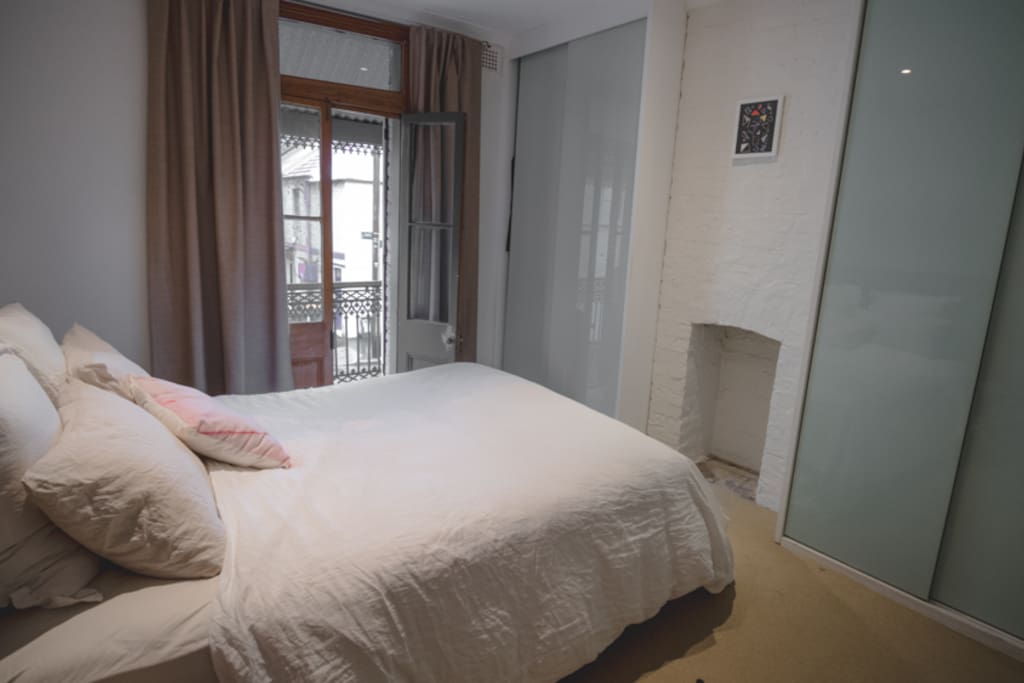 Bright bedroom with ceiling fan and balcony overlooking the tree-lined street.