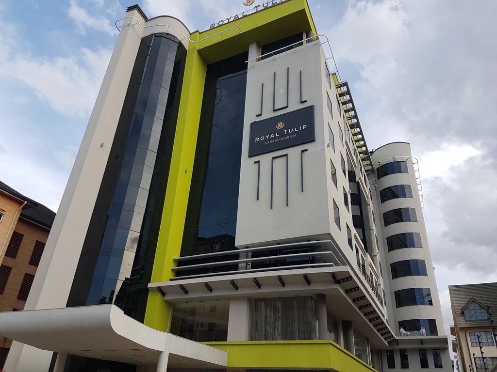 The exterior of the Royal Tulip Canaan Nairobi is showcased, featuring a modern architectural design with large glass panels and a striking yellow accent. The building stands five stories high, and the logo is prominently displayed at the top, contributing to the contemporary urban aesthetic.