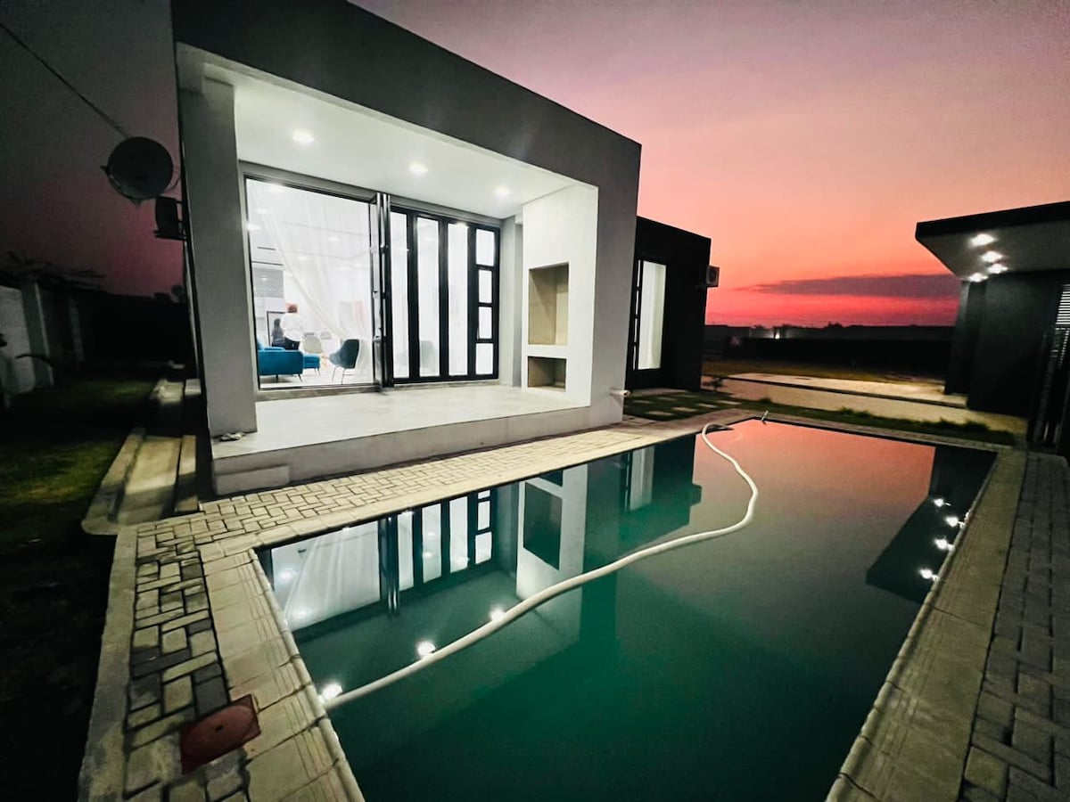 A modern apartment exterior is showcased at dusk, featuring a private swimming pool that reflects the colorful evening sky. Large glass doors provide a glimpse of the interior, enhancing the seamless connection between outdoor and indoor spaces.