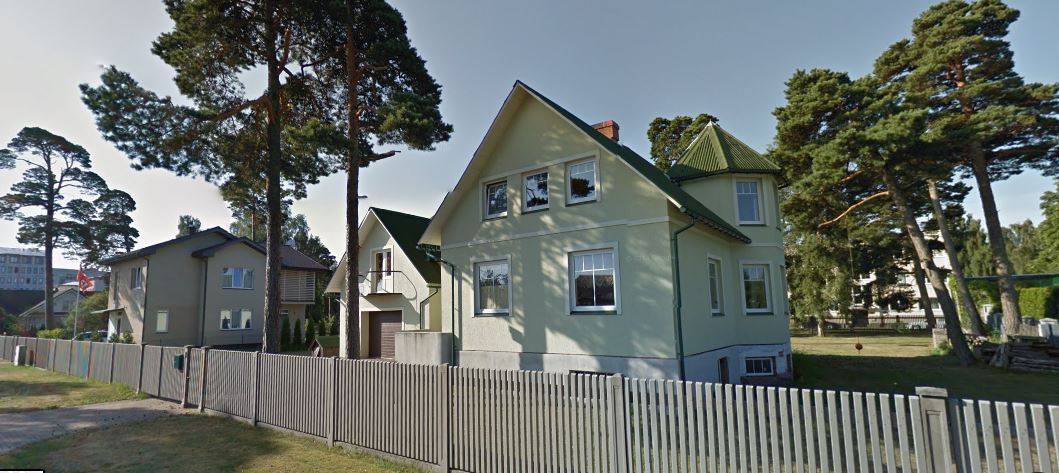 A spacious two-story house is depicted, featuring a light green exterior and traditional roof style. Tall trees surround the property, while a white fence delineates the yard, providing a sense of privacy. The house shows multiple windows, offering natural light and a welcoming facade.