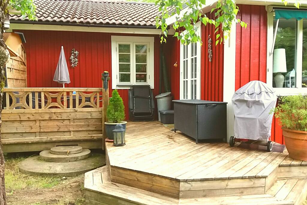 Terrass med bord stolar, dynor, filtar parasoll, grill och en låda med uteleksaker.