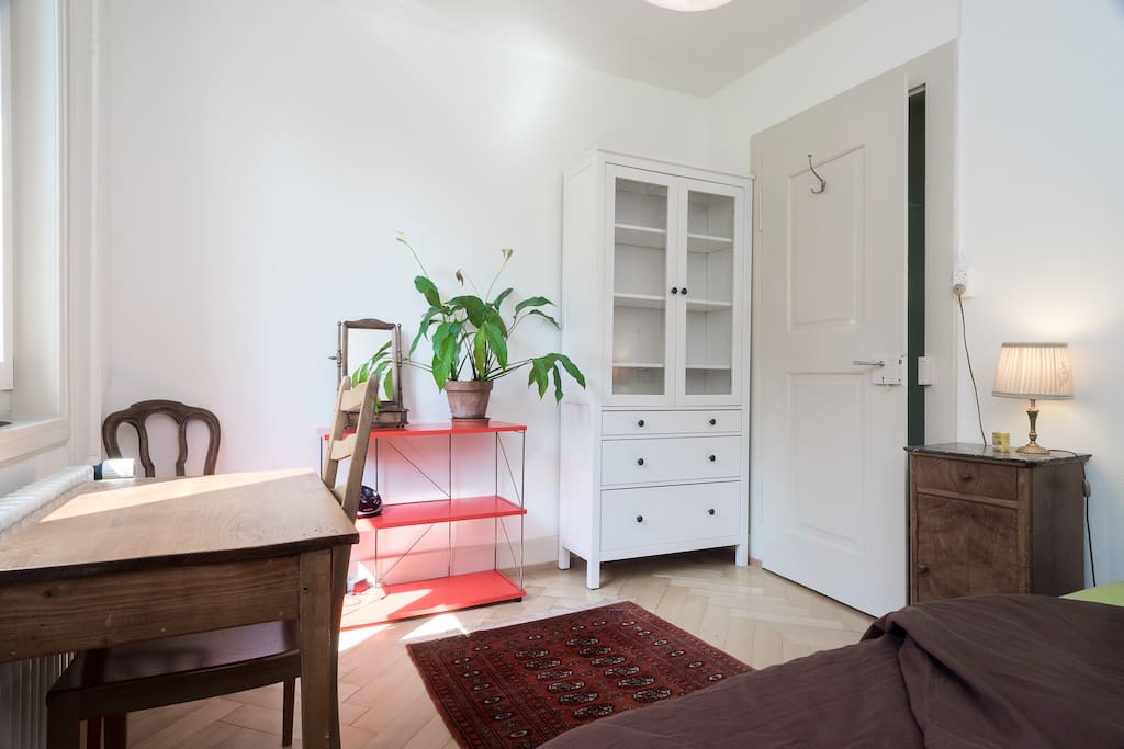 Guest room furnished with double bed, nightstand, closet, shelf, desk and clothes rack.