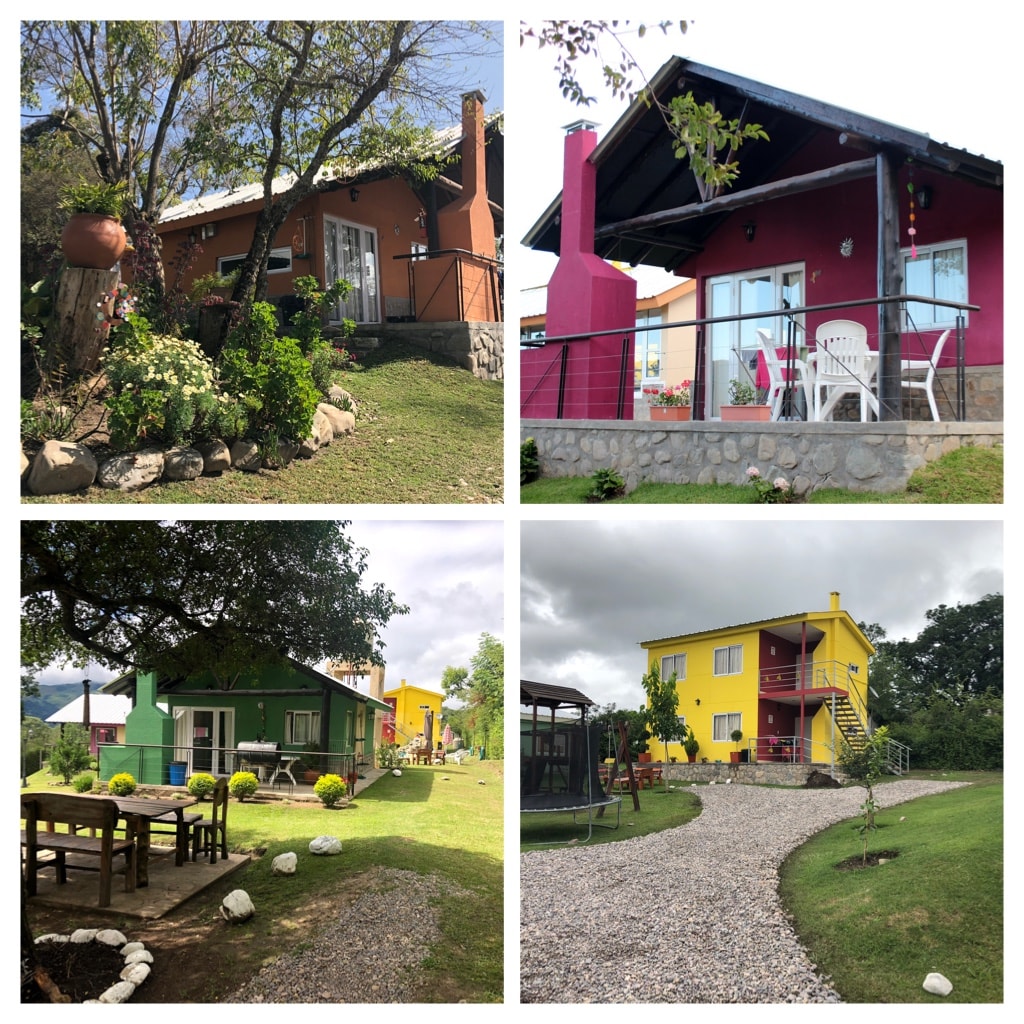 Four colorful cabins are displayed in this image, each featuring unique designs. The surroundings feature well-maintained gardens with greenery and stone paths. Outdoor seating areas are visible, alongside a shaded patio table and a play structure, creating a welcoming atmosphere for relaxation and family gatherings.