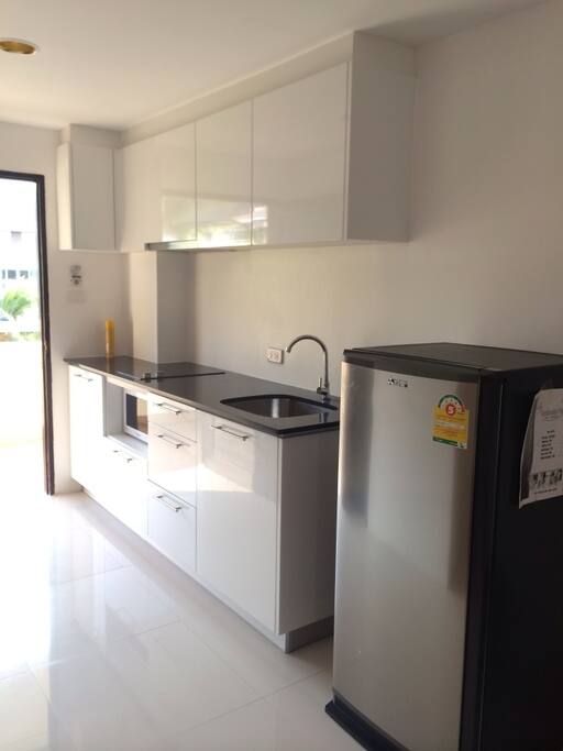 Kitchen corner with hob, hood, microwave, kettle, fridge and cutlery