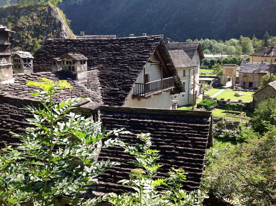 La casa, Ca' d' Bariff con i giardini vista dai grotti passeggiata dove si possono osservare in mezzo ai massi cantine con spazi esterni dove i privati durante la lavorazione del vino o la cura dei formaggi si rilassavano nelle calde giornate estive seduti ai tavoli di sasso. Sul fondo dell'immagine il museo.