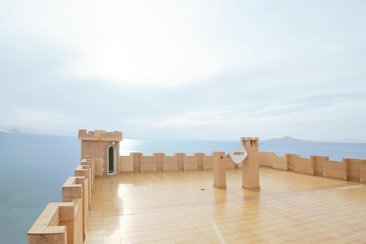 A spacious terrace is adorned with a smooth tile surface, featuring panoramic views of the sea. The raised walls provide a sense of enclosure, while a door leads to an enclosed area. The serene atmosphere is complemented by the horizon meeting the sky.