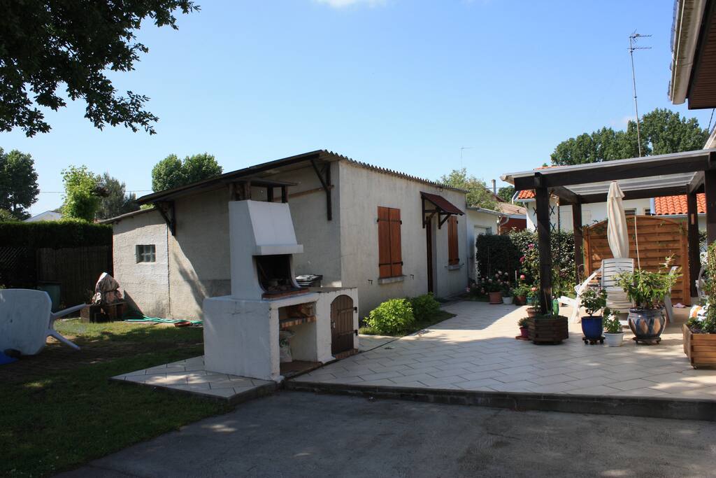 arrière de la maison avec terrasse et pergola couverte avec parasol et salon de jardin.