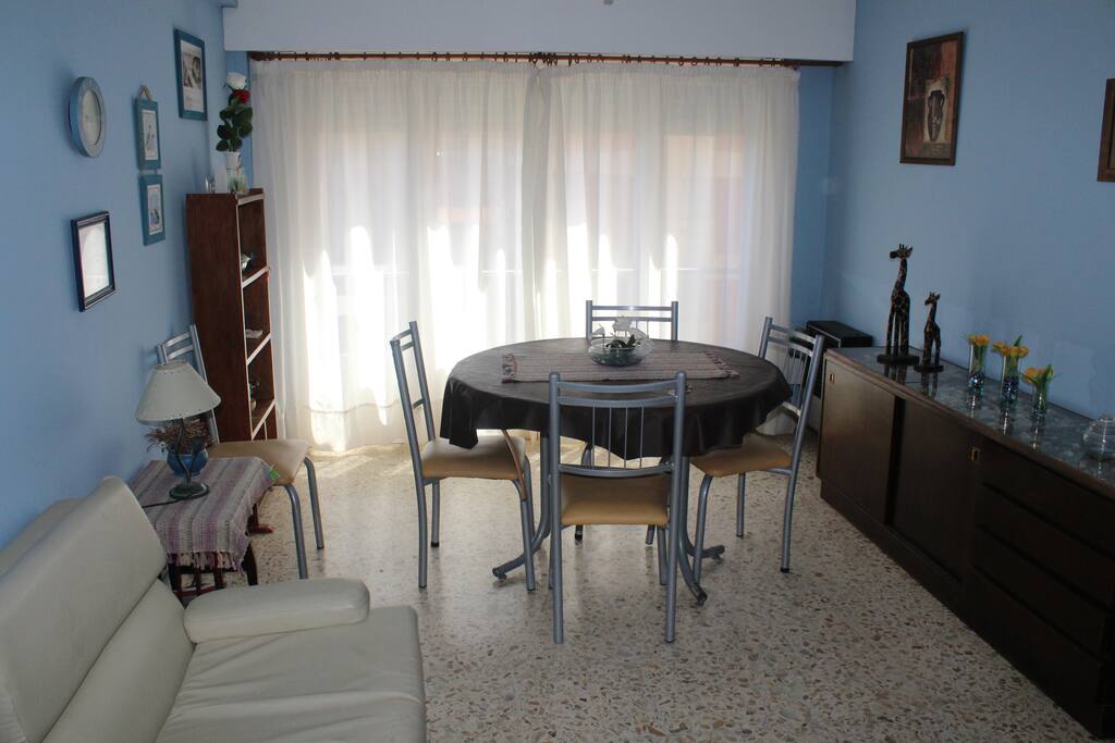 Living con balcom francés, mesa redonda con 4 sillas, velador y un sofá cama de una plaza
