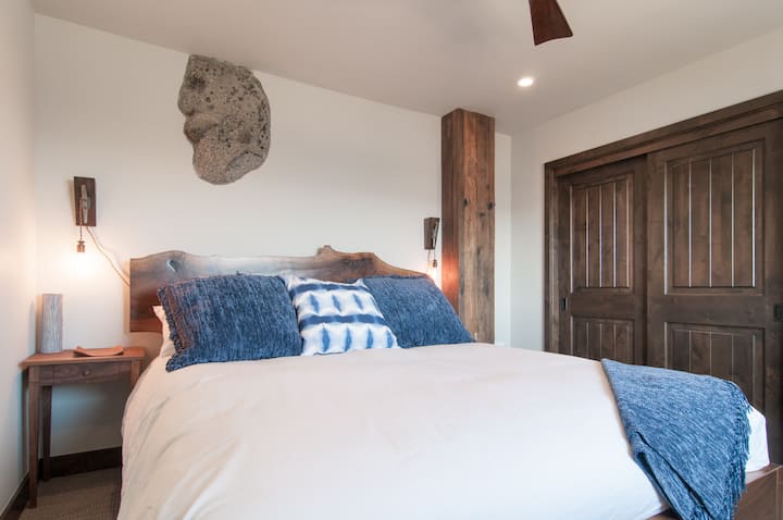 בחדר השינה הראשי למטה אתם יכולים לראות את הסלע יוצא מעל מיטת קליפורניה קינג סייז המותאמת אישית.