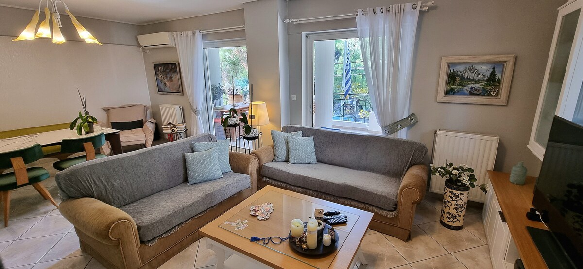 A welcoming living area showcases two comfortable sofas facing a central coffee table. Large windows allow natural light to illuminate the space, with soft curtains framing the views. A plant adds a touch of greenery, enhancing the overall ambiance of the room.