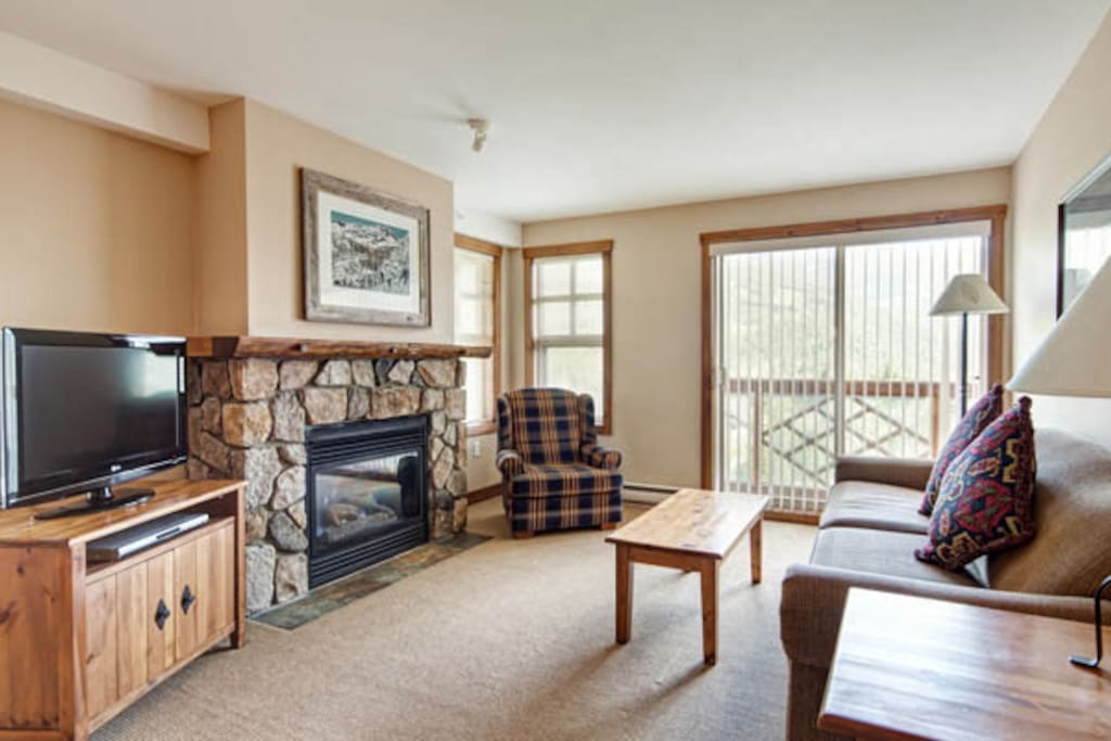 The cozy living room features large windows and a fireplace