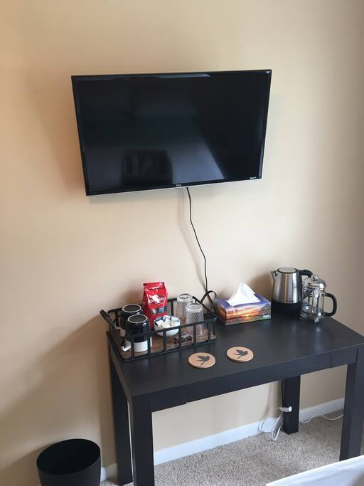 RokuTV in the bedroom with coffee station, desk, chair, lamp and comfortable bed.