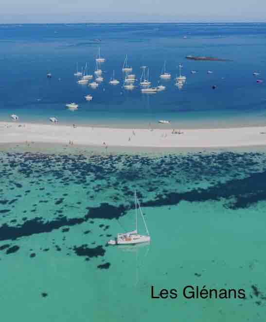 Aerial view of a serene coastline featuring a sandy beach and a vibrant blue sea. Small boats and sailboats are anchored in the clear waters, while gentle waves create a calming pattern along the shore.