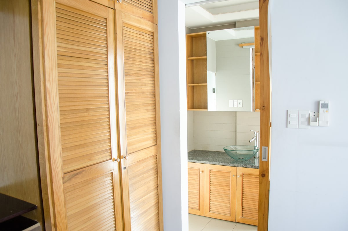 A clean and well-lit bathroom area is highlighted, featuring wooden cabinetry with slatted doors. A modern sink with a glass basin is positioned atop a granite countertop, with shelving units providing additional storage space.
