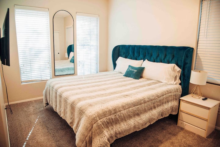 Dormitorio 3 "Glam" con TV inteligente, mesitas de noche, lámpara, armario y vestidor. Ropa de cama adicional, almohadas, cuna portátil, lavandería y baño en el pasillo adyacente. 