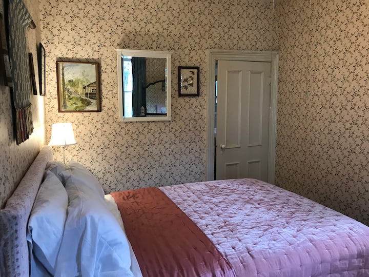 This traditional bedroom features period appropriate Thomas Strahan Rose wallpaper. Velvet bedding and drapes add a touch of luxury. This bedroom has a queen bed. 