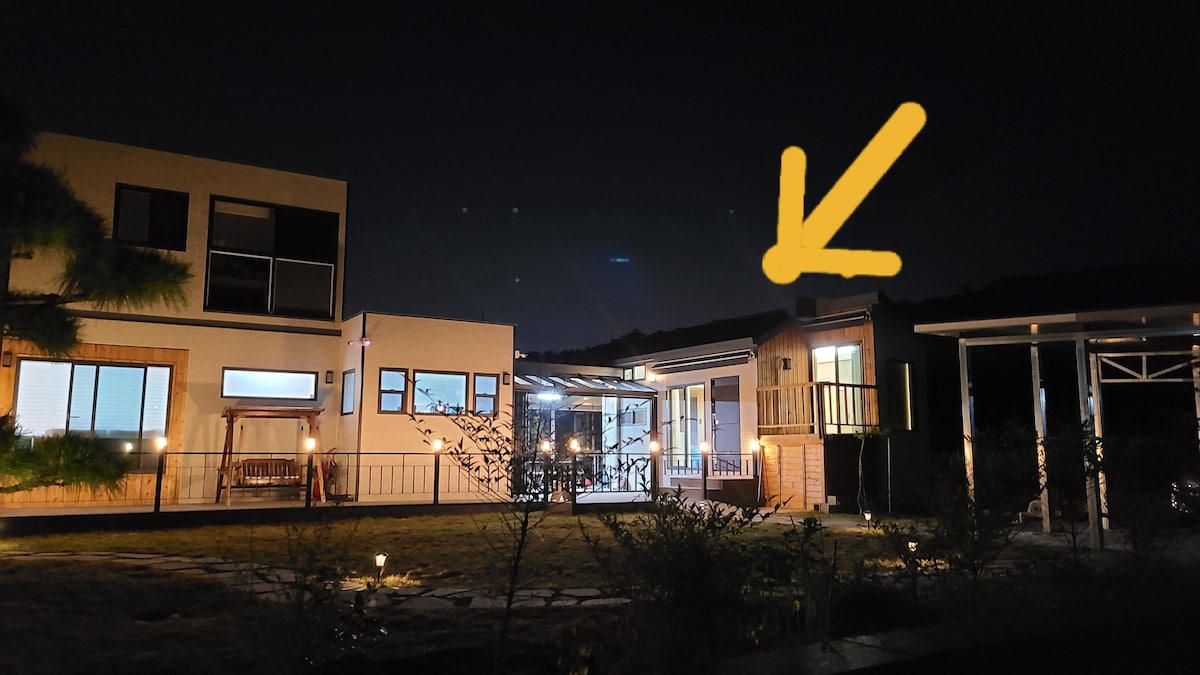 A quiet night scene showcases a spacious property with various structures. Soft lighting highlights the main building and a separate unit, while the surrounding garden is visible with pathways and greenery.