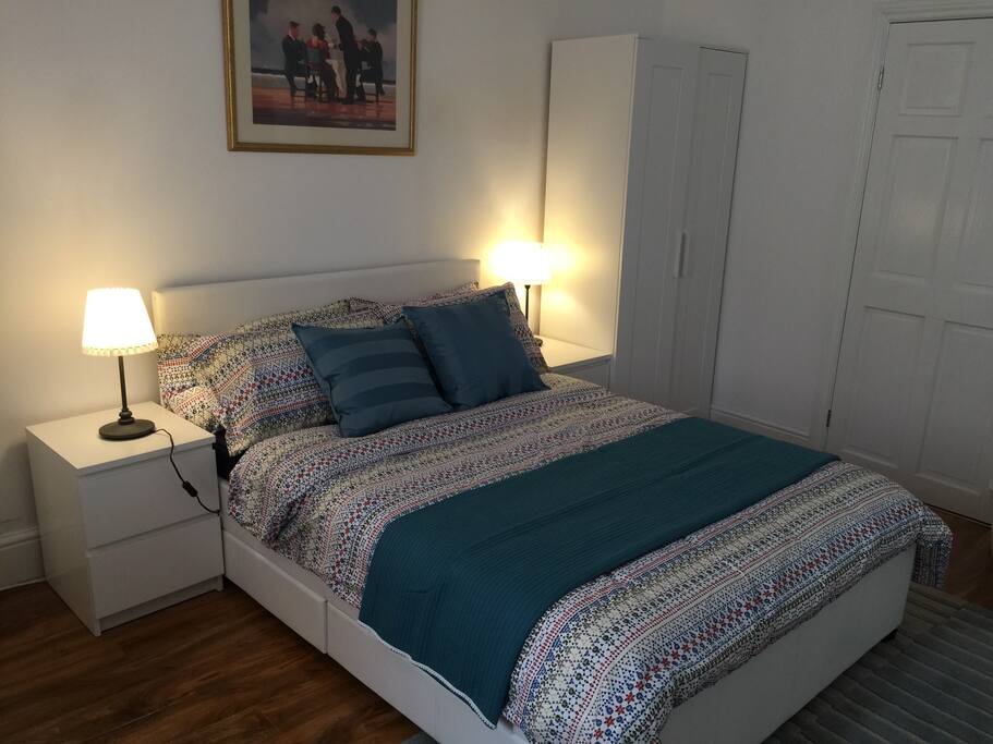 Part of the bedroom showing dressed double bed, bedside tables and lamps and wardrobe. Part of the door to the private shower and toilet is also shown.