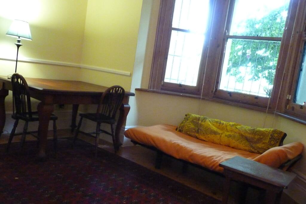 Cosy lounge with bay window looking out over leafy stoep area.