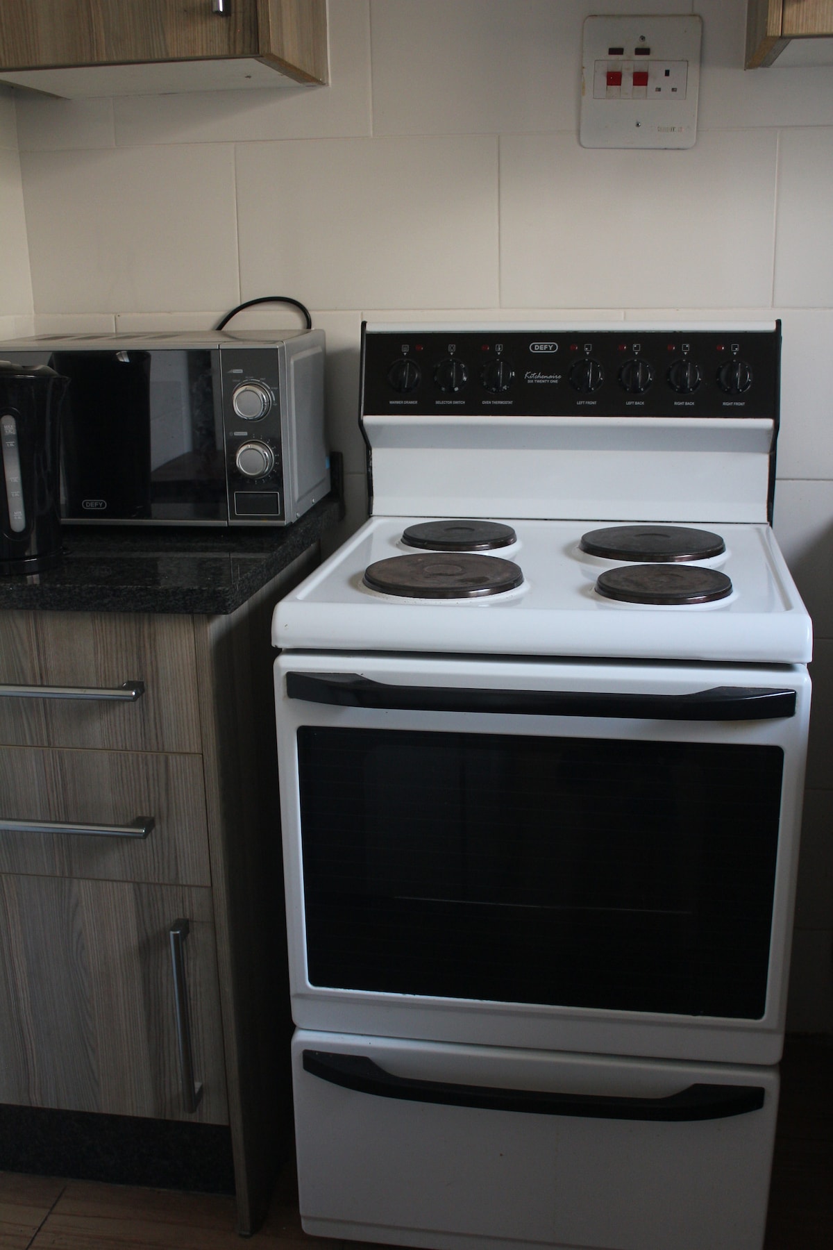 A compact kitchen area features a white stove with four burners and an oven below. To the side, a microwave on the countertop offers additional cooking options. Light wood cabinetry complements the dark granite surface, providing a modern and functional space.