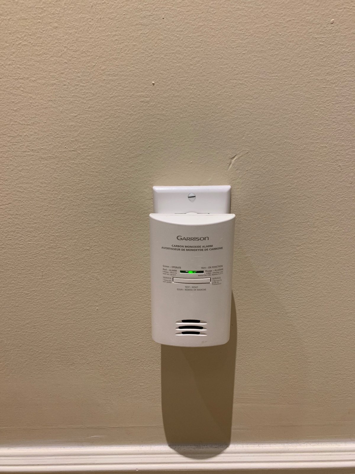 A white wall-mounted device is displayed against a light-colored wall. The device features a small green indicator light and has ventilation grilles at the bottom, suggesting functionality for air quality or environmental monitoring.