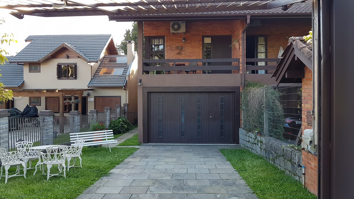 A well-maintained exterior features a private entrance leading to a charming guest house. The driveway is paved with stone, flanked by a manicured lawn. A white outdoor seating area is visible, alongside a two-car garage and a balcony enhancing the overall appeal of the property.