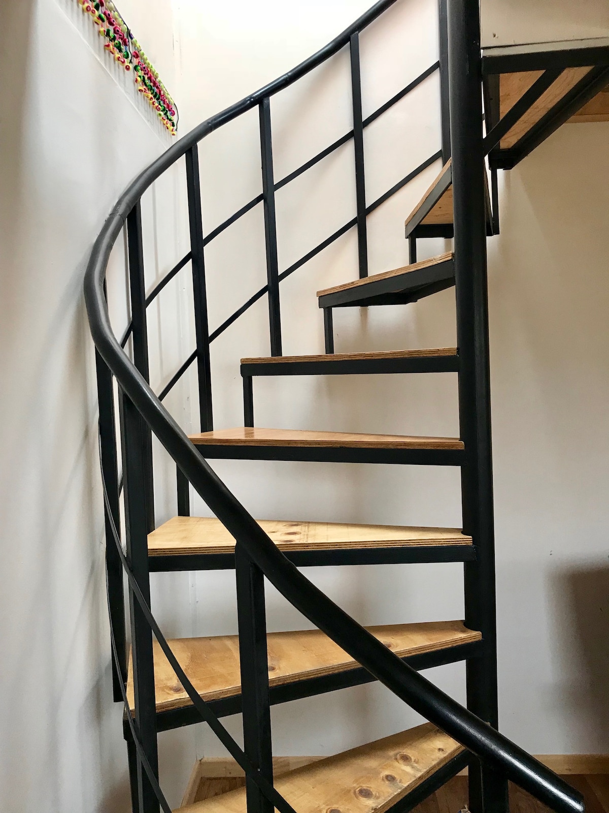 A spiral staircase with wooden steps and a black metal railing leads to the upper level. The design features a minimalist aesthetic, with the staircase seamlessly integrated into the surrounding walls.
