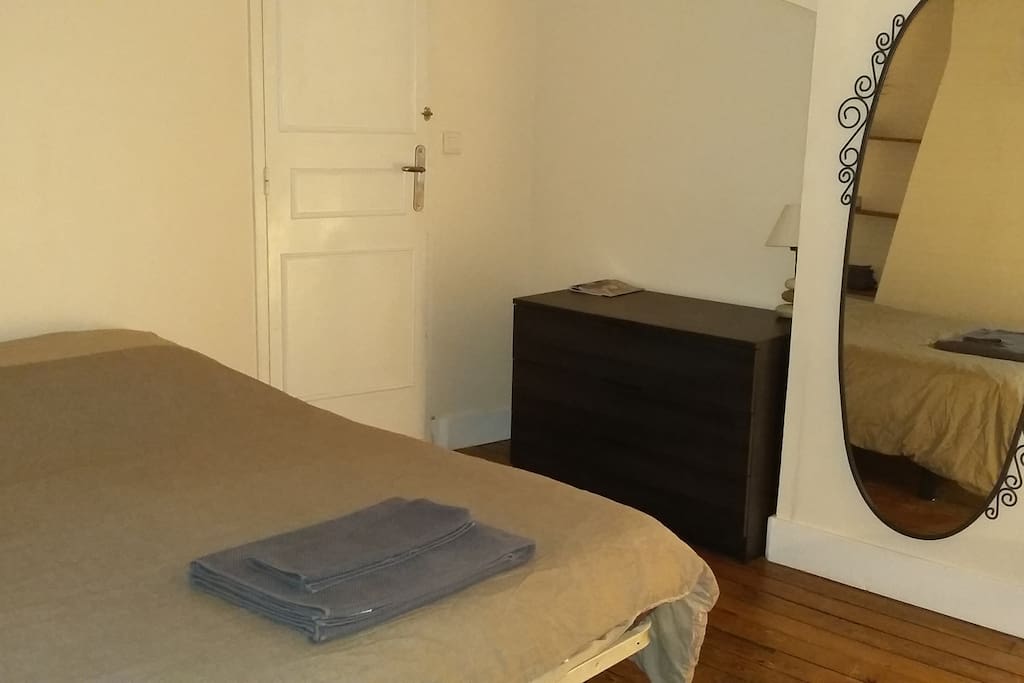 La chambre mansardée avec un velux, bureau, rangements, miroir, draps, serviette.