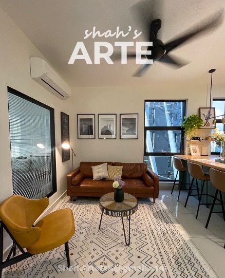 A living area features a brown leather sofa paired with a round coffee table, complemented by two yellow armchairs. Artwork is displayed on the walls, and natural light flows through large windows, enhancing the inviting space.