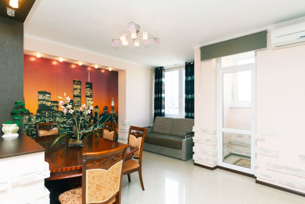 A cozy kitchen area separated by a partition with access to a glass balcony, with air conditioning above the balcony door, a dining wooden table, 4 chairs, a comfortable sofa bed can be used as an extra bed.