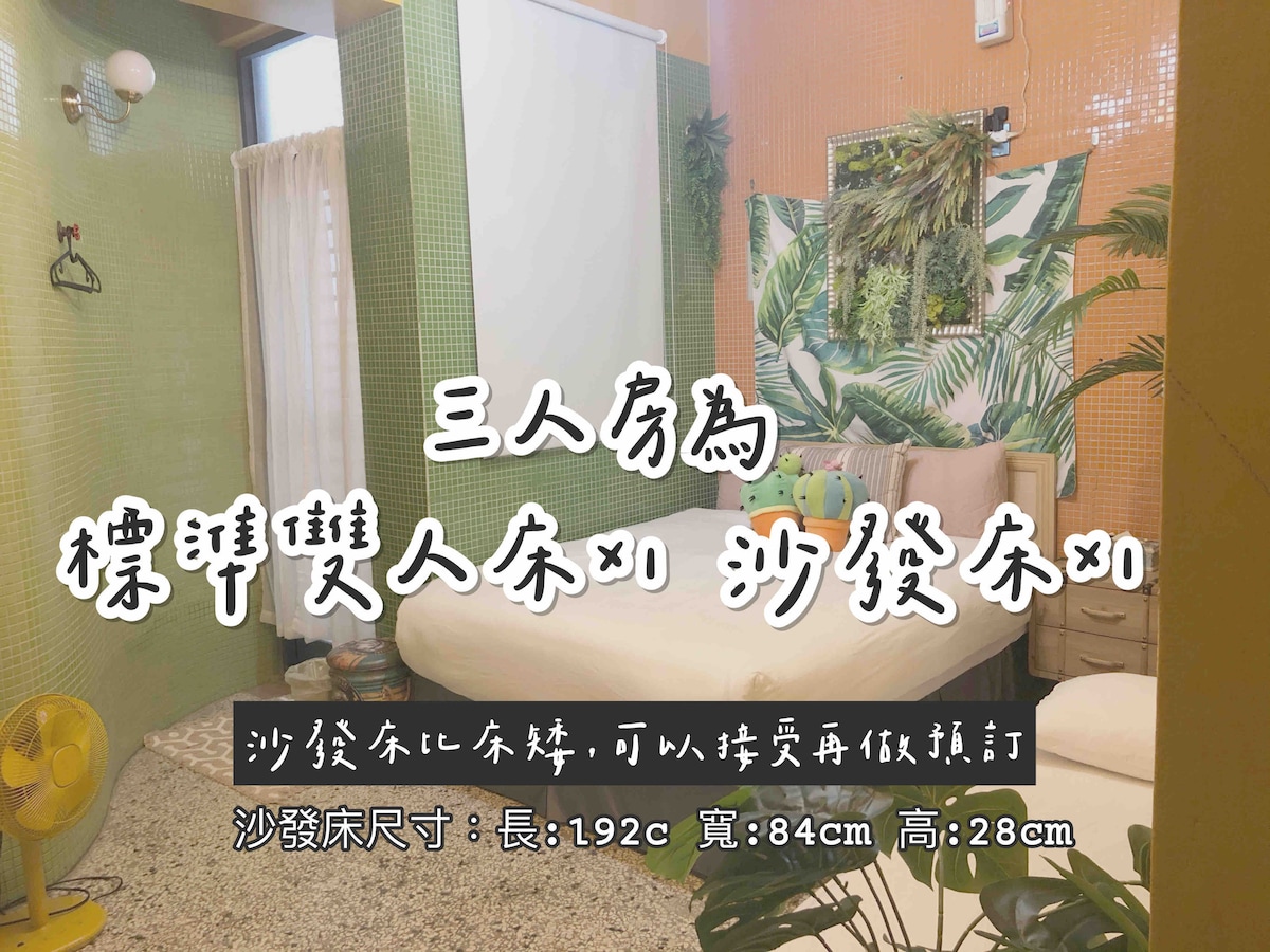 A cozy sleeping area features a spacious bed with a soft comforter and colorful pillows. A sofa bed suitable for additional guests is also present. The room is adorned with vibrant green and orange tiles, complemented by natural light filtering through a nearby window.