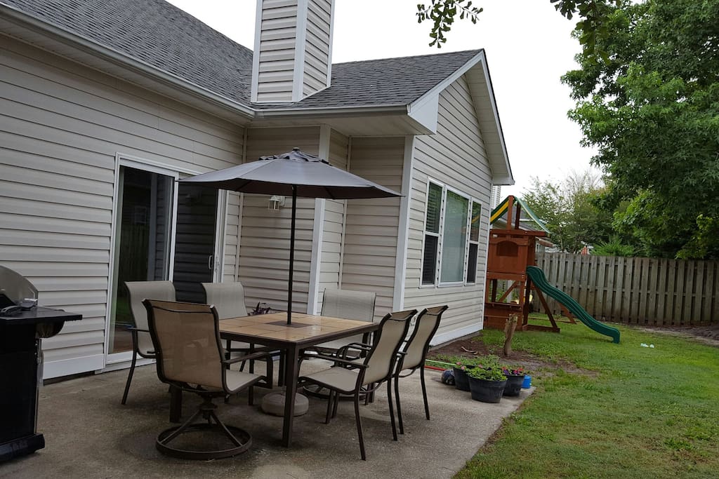 Back yard with patio, play set, and grill.