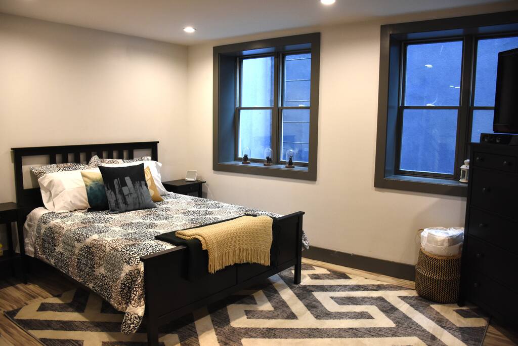Queen sized bed with nightstands including a noise machine, alarm clock, and earplugs.