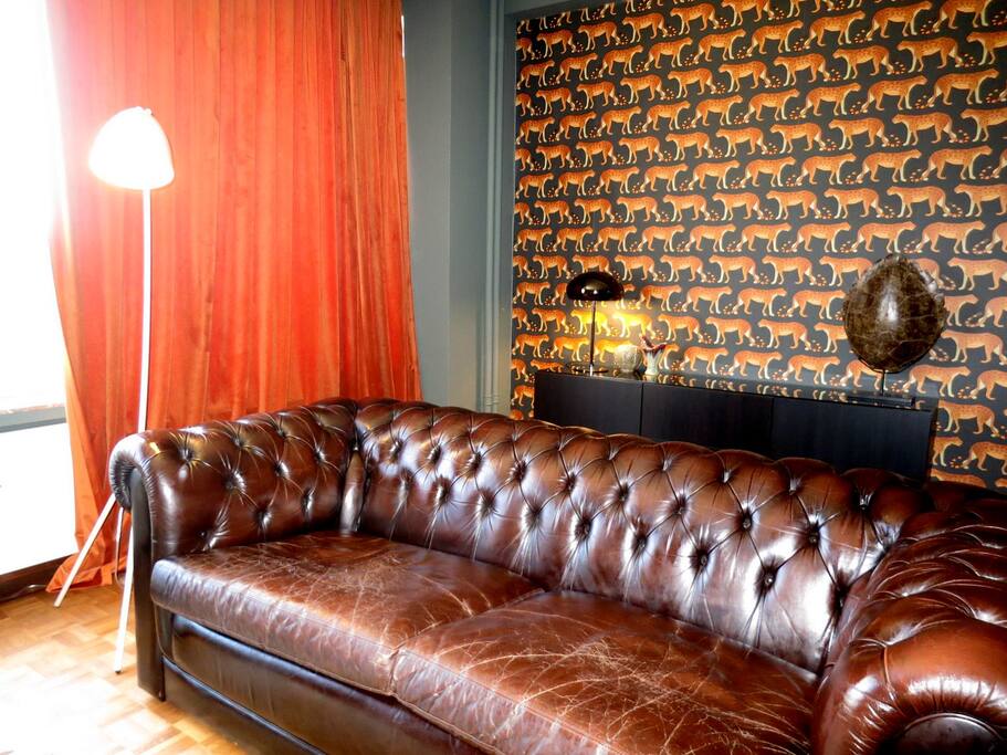 The large living room is richly decorated with a large Chesterfield and full length curtains.
