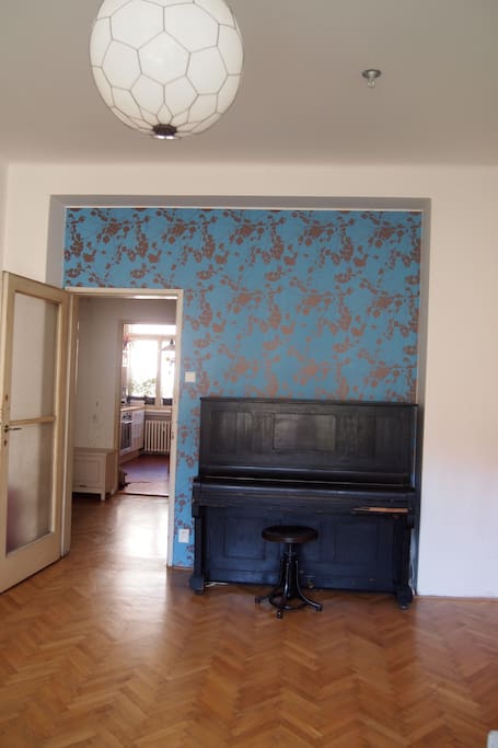 Living room - French window facing courtyard with park and barbecue area, lots of light and sunshine, private entrance from the hall. Piano, sofa, table, lamp, wardrobe and other equipment.