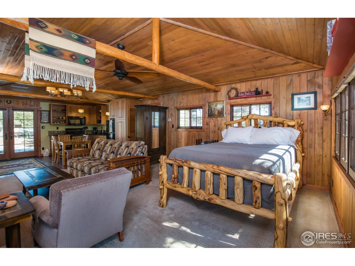 Comfortable queen bed in a spacious open floor plan with log beams.