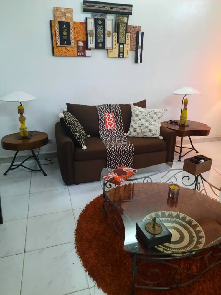 A comfortable seating area is presented, featuring a brown couch adorned with a patterned throw. Two side tables with yellow lamps are positioned beside the couch. A round glass coffee table displays decorative items, while a textured orange rug adds warmth to the space.