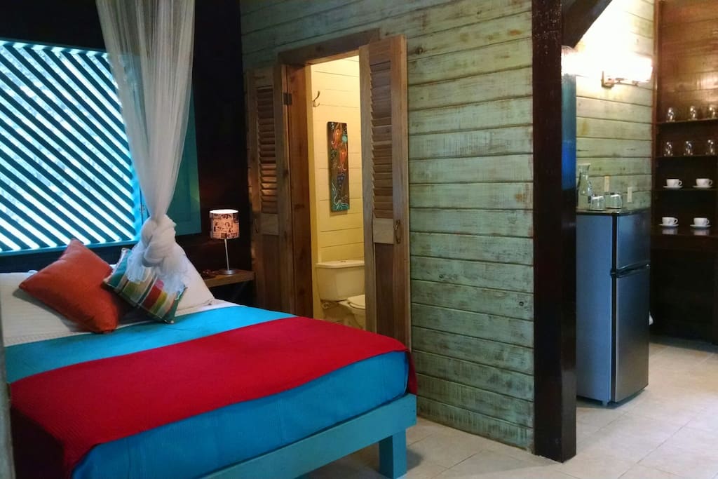 Interior view of bed, kitchenette, door to private bathroom.