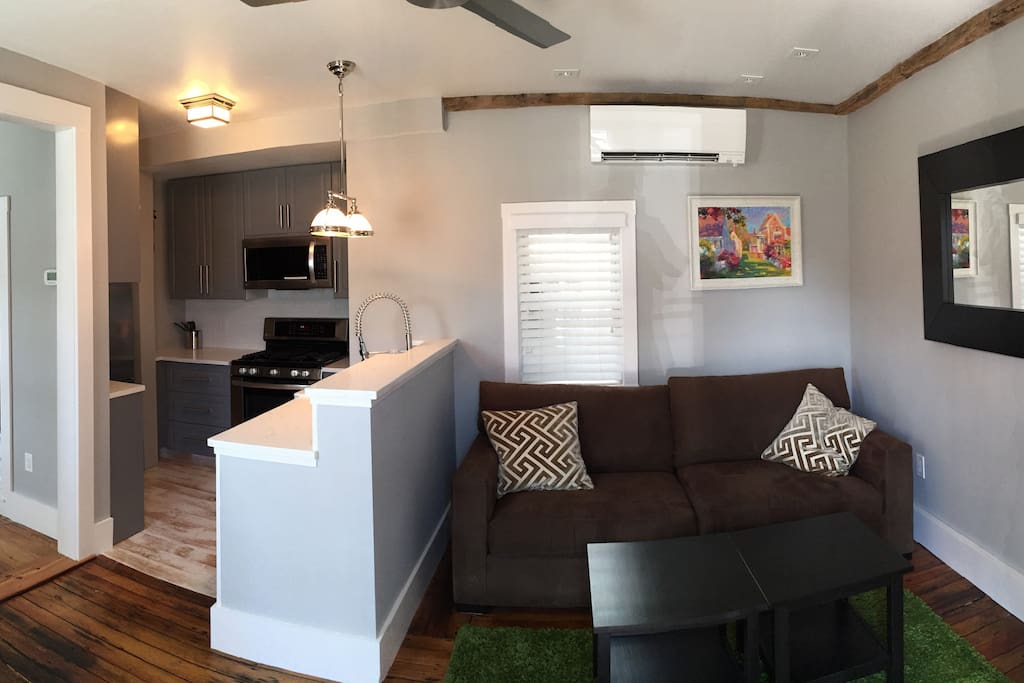 Panoramic shot of living room seating area, as well as the kitchen and entrance to bedroom (on the left).